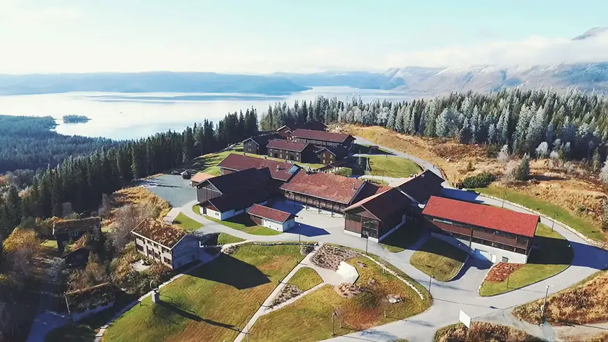 Oversiktsbilete av Rehabiliteringssenteret AiR, med bygningar i forgrunnen, og skog, fjell og vatn i bakgrunnen.